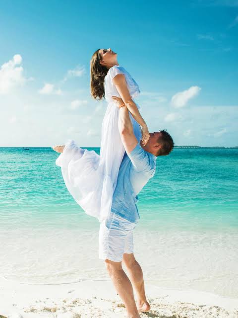 Honeymoon couple in white on a turquoise Sri Lankan beach, groom lifting bride by the shoreline