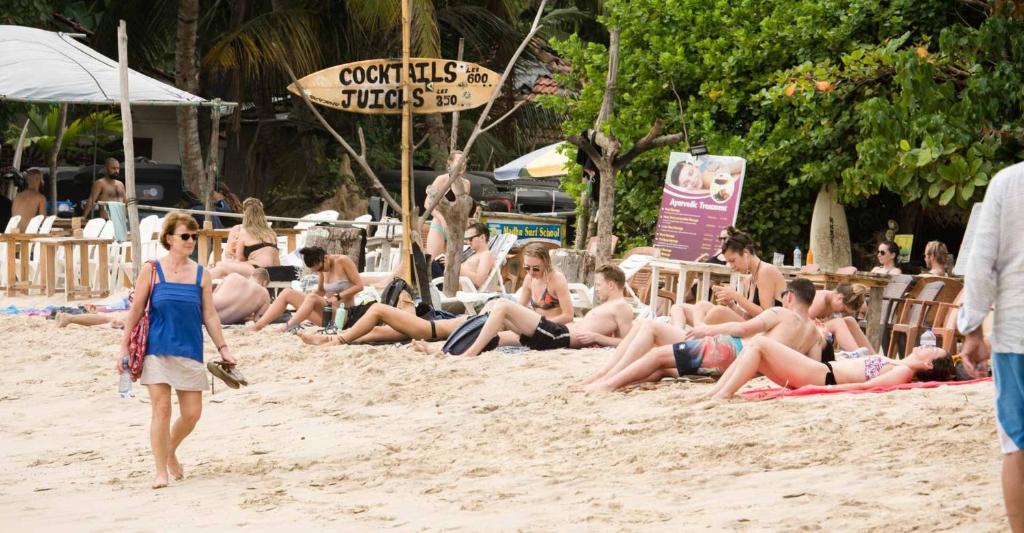Travellers relaxing on a busy palm-fringed beach in Sri Lanka, including a woman walking alone along the sand
